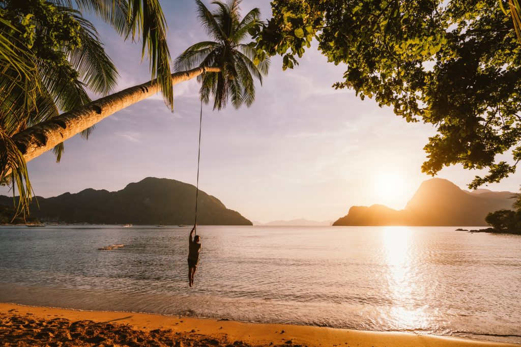 Silhouette of swing men with sunset over tropical island in background. El Nido bay. Philippines