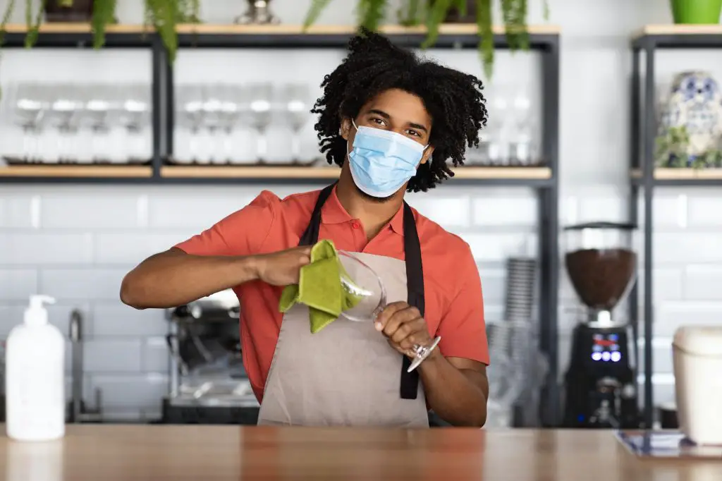 Work During Pandemic. Young black bartender wearing medical mask standing at bar counter